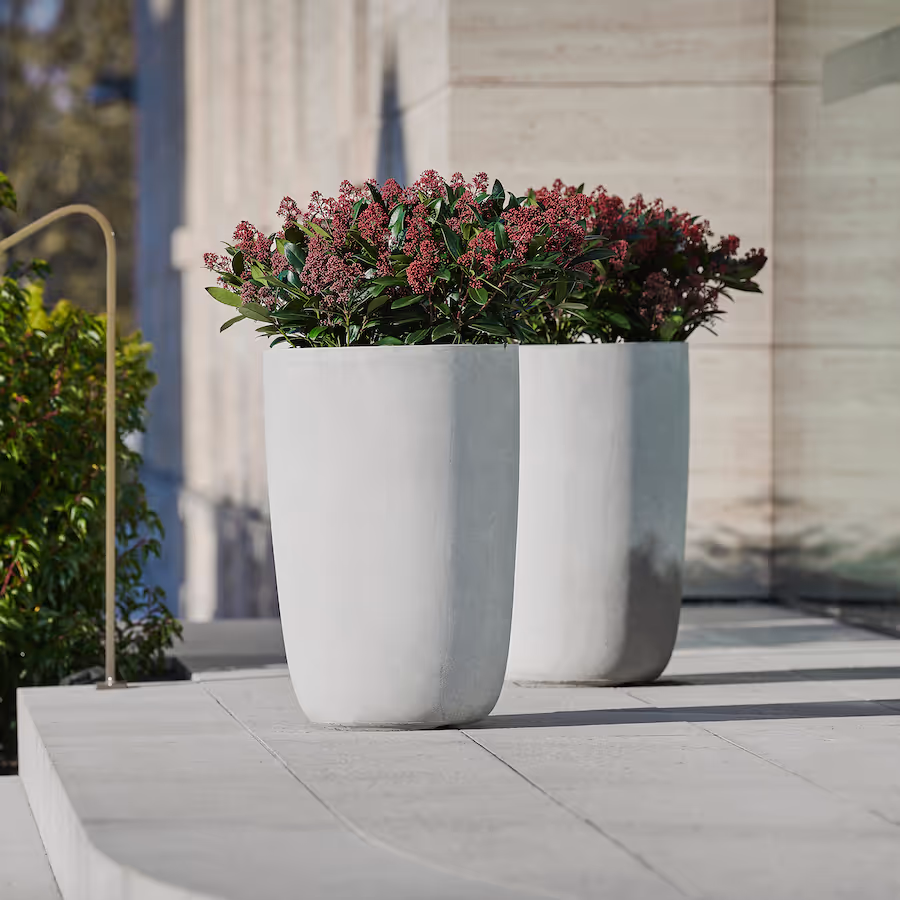 Zwei naturgraue Swisspearl Geisha Pflanzgefäße mit roten Blumen auf der vorderen Terrasse.