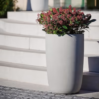 Naturgraues Swisspearl Geisha Pflanzgefäß mit roten Blumen vor Treppen.