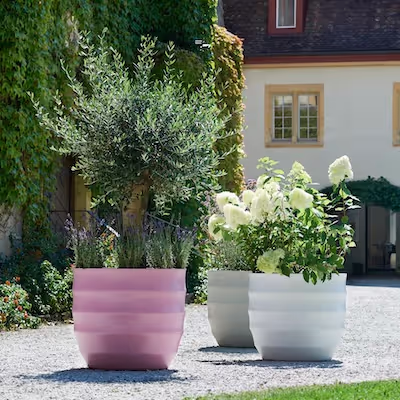 Weiße und rosa Swisspearl Hive Pflanzgefäße mit Blumen und Baum im Garten.