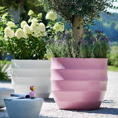 Weiße und rosa Swisspearl Hive Pflanzgefäße mit Blumen und Baum im Garten.