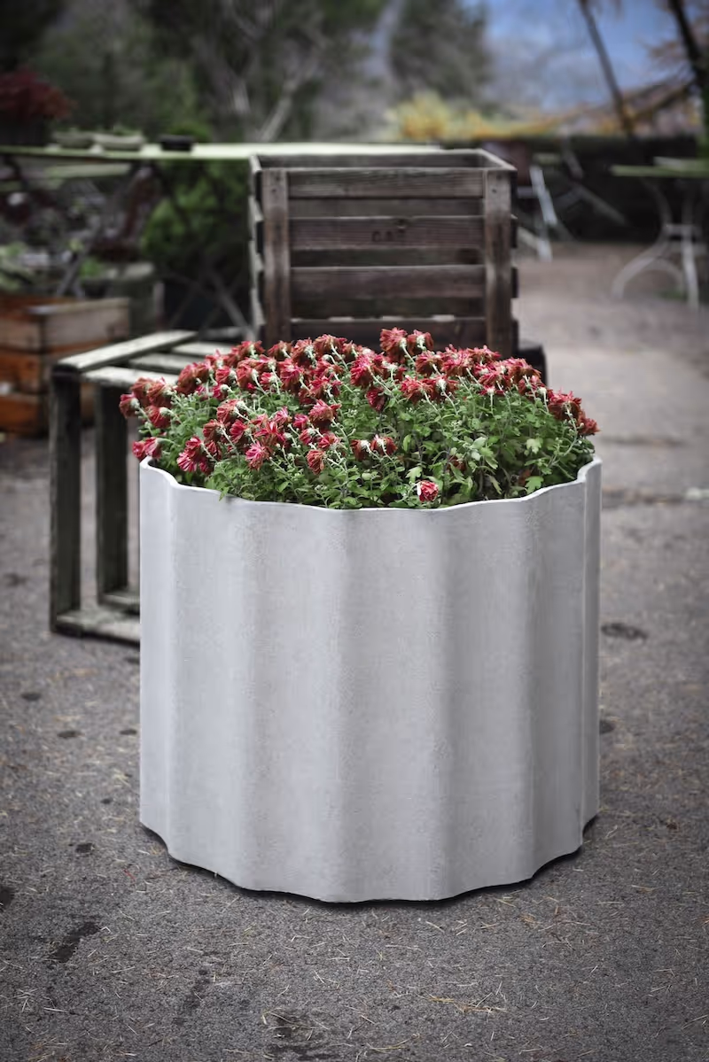 Weißes Swisspearl Kolonna Pflanzgefäß mit Blumen.